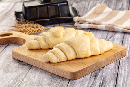 Freshly baked croissants on a wooden cutting board with wheat ears.の写真素材