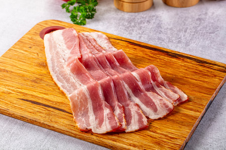 Raw bacon pork meat slices over board