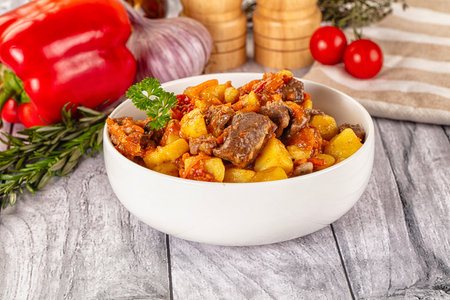 Fried potatoes with meat and vegetables in a bowl on wooden backgroundの写真素材