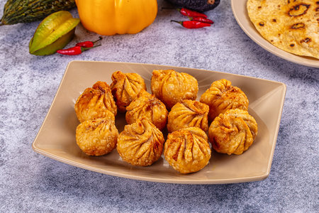 A high-angle view of delicious fried dumplings momos, in a black pan. Surrounded by colorful fresh vegetables and flatbread on a grey textured background. Appetizing food still life.の写真素材