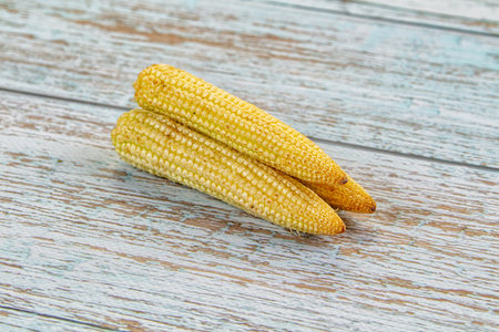 Top-down view of several fresh, yellow baby corn cobs arranged on a textured slate background....