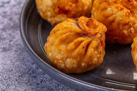 A high-angle view of delicious fried dumplings momos, in a black pan. Surrounded by colorful fresh...
