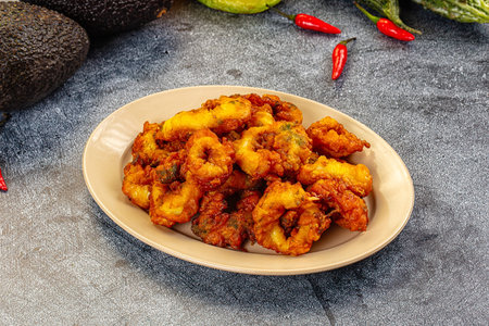 Appetizing platter of golden fried calamari rings. Savory seafood dish on a plate against a dark background, garnished with fresh red chilies and avocado. Bright, clean food photography.の写真素材