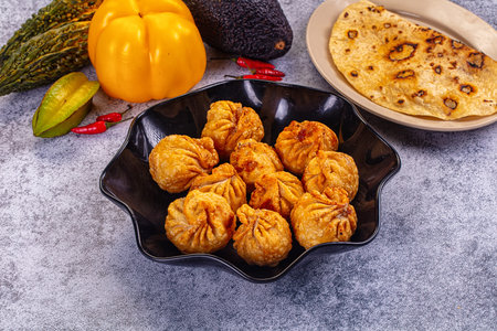 A high-angle view of delicious fried dumplings momos, in a black pan. Surrounded by colorful fresh vegetables and flatbread on a grey textured background. Appetizing food still life.の写真素材
