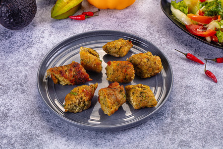 Close-up of baked chicken and vegetable fritters on a rustic plate. The scene includes fresh salad,...