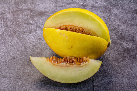 A fresh, ripe yellow melon, cut open with a juicy slice in the foreground. The seeds are visible...