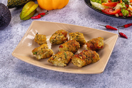 Close-up of baked chicken and vegetable fritters on a rustic plate. The scene includes fresh salad,...