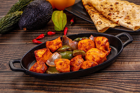 Close up of Paneer Tikka, a traditional Indian dish with cottage cheese, peppers, and onions. Served with roti flatbread. Vibrant orange and green colors on a dark wood background. Appetizing food.の写真素材