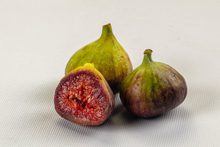 Close-up of fresh green and purple figs on a textured surface. One fig is sliced open, revealing its...