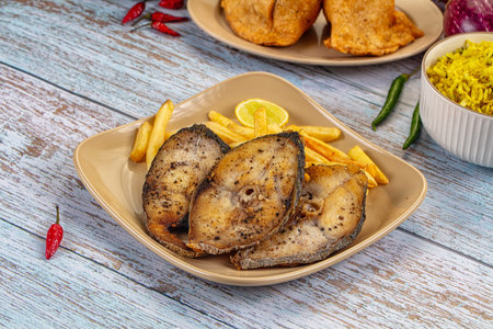 Pan-fried King fish steaks and golden french fries on a white plate with a lemon wedge. Served on a...