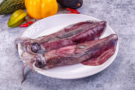 Raw squid on a plate surrounded by colorful vegetables. High-angle still life with fresh calamari,...