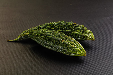 Still life of fresh, raw bitter melons on a dark textured background. The green, bumpy vegetables,...