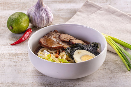 A warm bowl of Asian ramen noodle soup with tender beef, nori, a hard-boiled egg, and fresh spring...