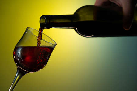 red wine is poured from a bottle into a glass. Nice close up shot on yellow-green backgroundの写真素材