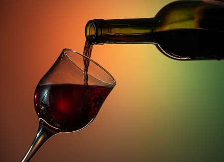 red wine is poured from a bottle into a glass. Nice close up shot on yellow-green-orange backgroundの写真素材