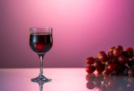 One glasse of red wine and bottle on the fantastic pink backgroundの写真素材