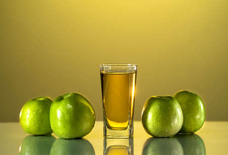 green apples lie on the table with a reflection. next to it is a glass of apple juice. sunset backgroundの写真素材
