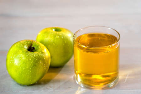One glass of apple juice with green apples in the sunset background. Nice white wood table. Summer...