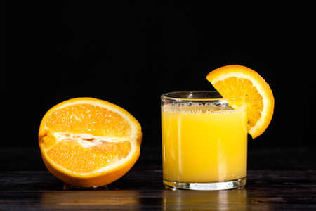 A ripe sliced orange and a glass of juice on a wooden background. close-up. healthy lifestyle. healthy eating. vitaminsorange slice on a glass of juiceの写真素材