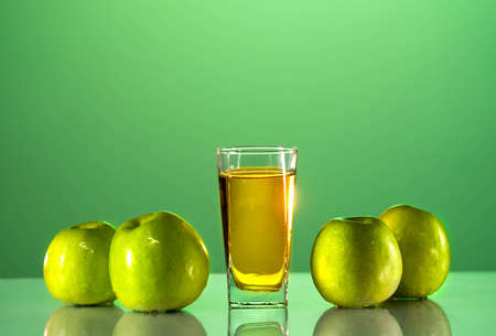 Green apples lie on the table with a reflection. next to it is a glass of apple juice. Green backgroundの写真素材