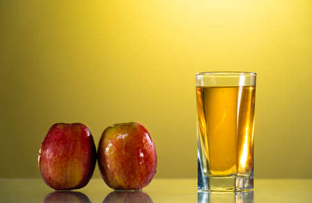 One glass of apple juice with red apples in the sunset background. Reflected surface. Summer day. Good mood.の写真素材