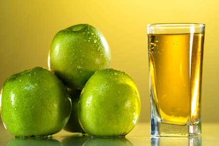 One glass of apple juice with green apples in the sunset background. Reflected surface. Summer day. Good mood.の写真素材