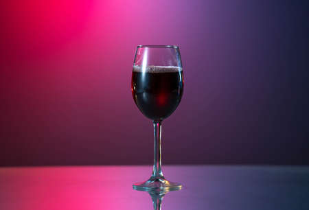 red wine is poured from a bottle into a glass. on the table with reflected surfaceの写真素材