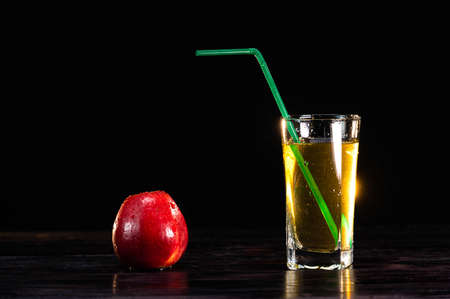 A ripe red apple and a tall glass of juice with a straw on a wooden background. close-up. healthy lifestyle. healthy eating. vitaminsの写真素材