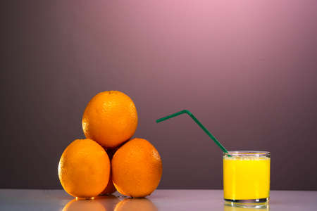 a glass of organic fresh orange juice and some oranges on the reflection table with thenice pink backgroundの写真素材