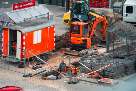 Urban Construction Site with Excavator, Worker, and Safety Barriersの写真素材