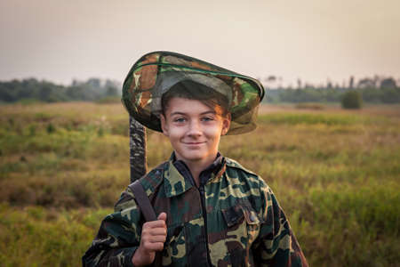 Young smiling boy with hunting shotgun standing at green field during sunsetの写真素材