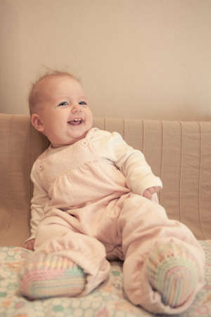 Funny smiling baby girl sitting on sofa on beige backgroundの写真素材
