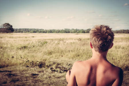 Young boy in a rural field looking into the distance. concept for future, discovery, exploring and educationの写真素材