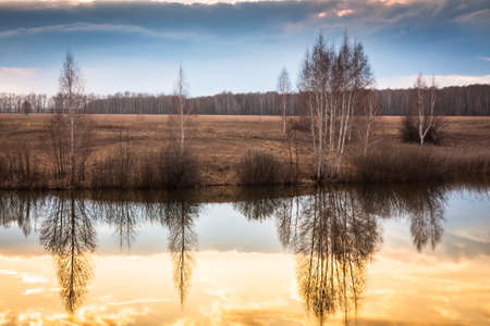Beautiful landscape with reflections on water during sunset ar river bank