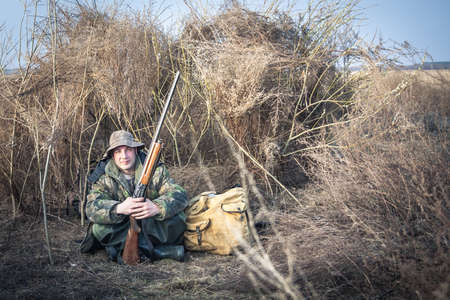 Hunter man with shotgun and backpack having a rest in rural field during hunt season