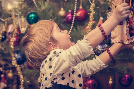 Happy child pulling hands to Christmas present and christmas tree on background