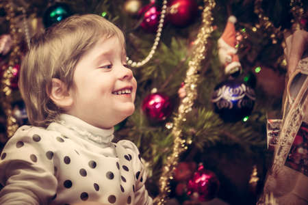 Happy smiling child getting Christmas gift with Christmas tree on background in retro styleの写真素材