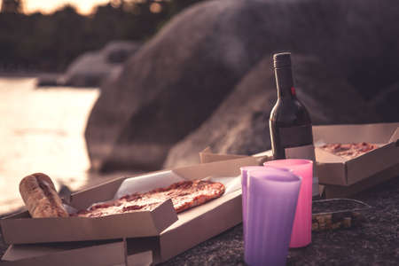 Picnic at tropical beach with wine and pizza during sunset by the seaの写真素材