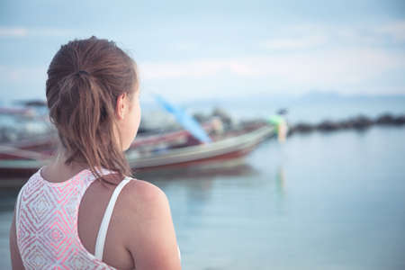 Teenager girl looking into the distance on tropical beach at sunset during summer holidays. Sunlight illuminate girl faceの写真素材