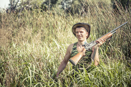 Hunter man in rural field with shotgun break through tall reed grass during hunting seasonの写真素材