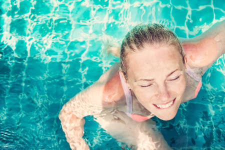 Young beautiful relaxed woman with closed eyes from pleasure enjoy swimming in turquoise water in swimming pool with copy space. View from aboveの写真素材