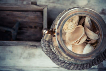 old vintage glass jar with sea shells on blurred wooden background with copyspace. Vintage tropical still lifeの写真素材