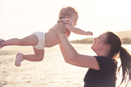 Child pulling his hand towards mother while playing at beach. Young happy mother catching child after throwing him up. Concept for happiness.の写真素材