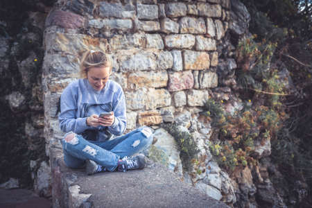 Young smiling woman relaxing outdoors with mobile phone in social media during her travelの写真素材