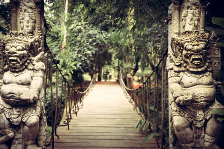 Pathway leading to tropical forest with terrible statues of Asian Buddhism demons on both sides in...