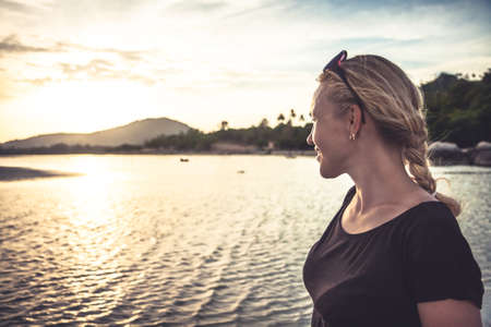 Young woman at tropical beach looking into the distance during beautiful sunset with copy spaceの写真素材