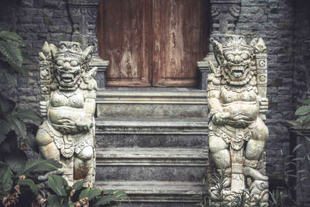 Ancient Asian demons deities at the enter to the old temple with old wooden door and stone steps in vintage styleの写真素材