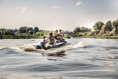 Group of men sailing on motor boat by river in summer day to the camping site during hunting seasonの写真素材