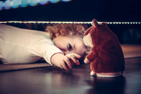 Playful cute curious baby pulling hand to toy under the bed in vintage styleの写真素材