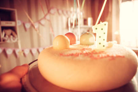 Hand  holding  happy birthday cake for children party decorated with one candle and sweet balloons in honour of first birthday anniversary as happy birthday backgroundの写真素材